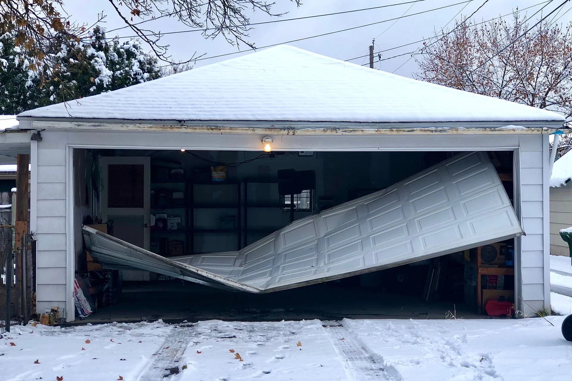 Damaged garage door surrounded by snow.